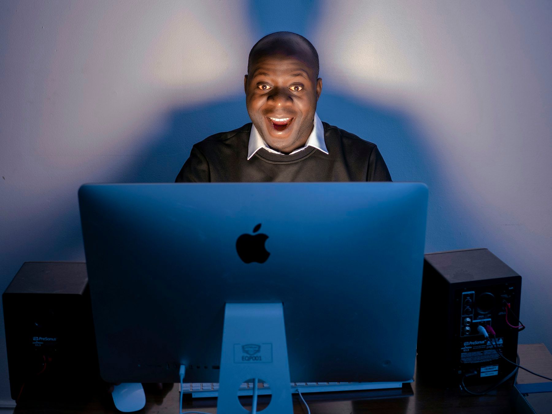 A man looks over his computer screen, delighted, in soft blue light.
